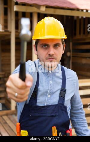 Bel giovane riparatore che tiene utensili da costruzione davanti a sfondo di legno Foto Stock