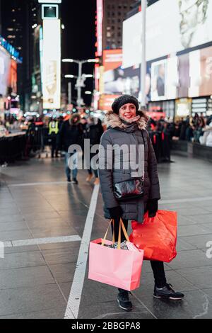 Donna con molte borse di shopping che guardano le luci e la folla in Times Square Foto Stock