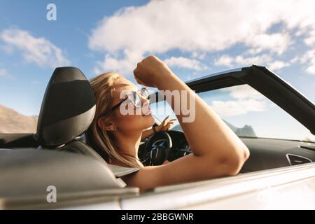 Donna attraente con occhiali da sole che viaggiano in un'auto convertibile. Donna su un viaggio in auto. Foto Stock