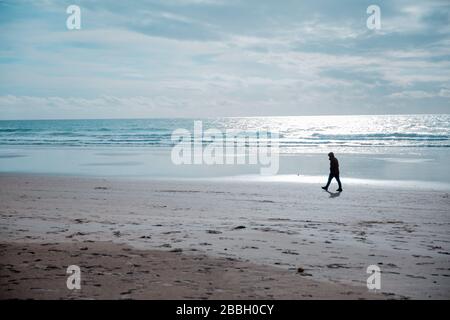 Silhouette di un uomo solitario su una spiaggia di sabbia con cielo blu e nuvole Foto Stock