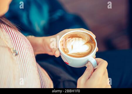 Giovane donna seduto e tenendo una tazza con caffè a forma di cuore in un caffè Foto Stock