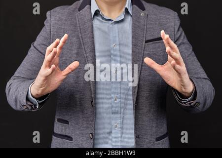 L'uomo in una giacca mostra con le mani un oggetto astratto. Primo piano. Foto Stock