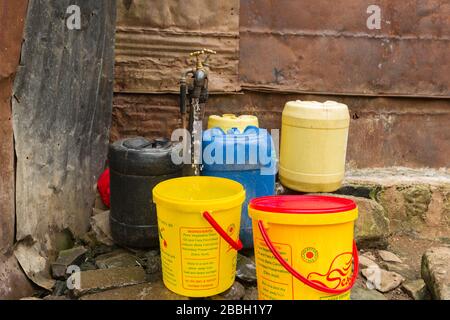 Diversi contenitori d'acqua in plastica intorno ad un rubinetto d'acqua all'aperto con acqua che sgocciola da esso, Nairobi, Kenya Foto Stock