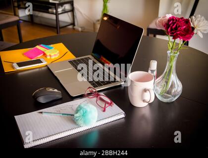 Lavorare da casa con una tastiera per computer portatile con tazza da caffè, mouse e blocco note su un tavolo da pranzo Foto Stock
