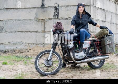 Una donna post apocalittica in moto vicino alla costruzione distrutta Foto Stock
