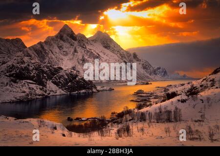 alberi di luce solare che splendono attraverso le nuvole sopra le montagne innevate intorno al fiordo. Foto Stock