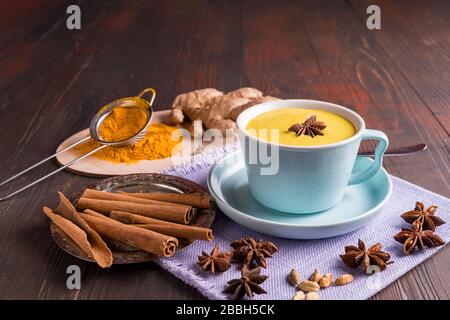 Latte curcuma ayurvedico dorato realizzato con curcuma e spezie, su sfondo ligneo. Bevanda sana di medicina. Foto Stock