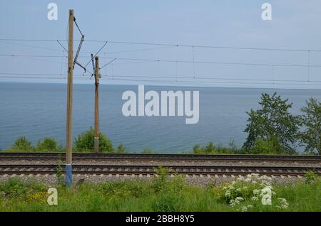 La ferrovia transsiberiana vicino alla città di Baikalsk sulla riva orientale del lago Baikal, Russia. Sullo sfondo si trova il lago Baikal. Foto Stock