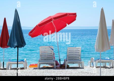 Ombrellone rosso e chaise per il relax e il comfort sulla costa del mare. Felice estate vacanze e concetto di turismo. Servizio a pagamento sulle spiagge del paesaggio acquatico. Foto Stock