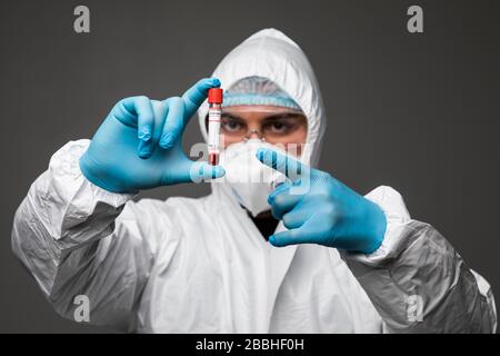 Pandemia di coronavirus. L'epidemia del Coronavirus cinese in un vestito protettivo esamina il virus in un tubo isolato su sfondo grigio Foto Stock