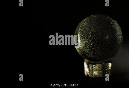 Sfera di cristallo su piedistallo con gocce d'acqua, sfondo nero Foto Stock