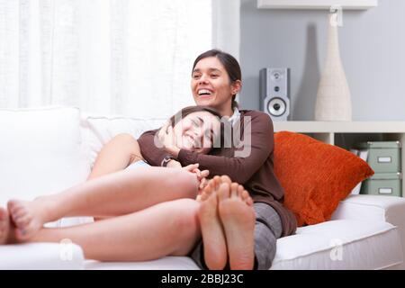 Ridendo giovane madre e figlia rilassarsi a piedi nudi su un comodo divano nel soggiorno abbracciando e sorridendo in un alto ritratto chiave con copia spa Foto Stock