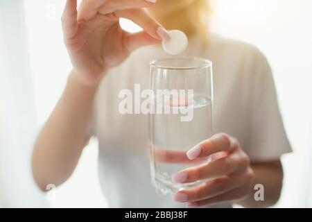 Giovane donna in camera durante la quarantena. Vista del taglio e primo piano delle mani tenendo la pillola per gettarla nel vetro con acqua. Impiccato o assassino del dolore. Foto Stock