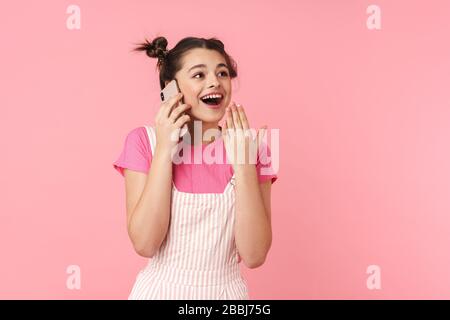 Foto di bella ragazza eccitata con anello naso parlare sul cellulare ed esprimere sorpresa isolato su sfondo rosa Foto Stock