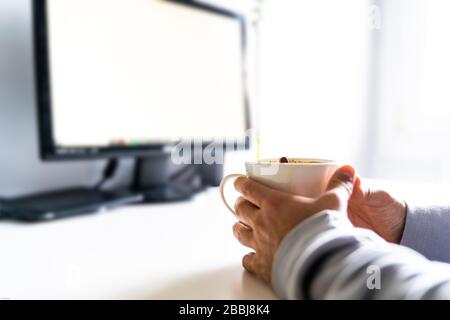 Persona che tiene una tazza da caffè davanti al computer su una scrivania. Foto Stock