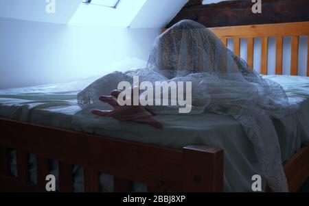 Una figura spettrale, spettrale e semi trasparente su un letto, con una mano che arriva in dolore Foto Stock