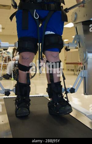 Vista parziale di un uomo in terapia fisica su una macchina che aiuta le gambe paralizzate a camminare Foto Stock