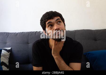 Un giovane ispanico seduto su un divano molto pensieroso che guarda fuori una finestra Foto Stock