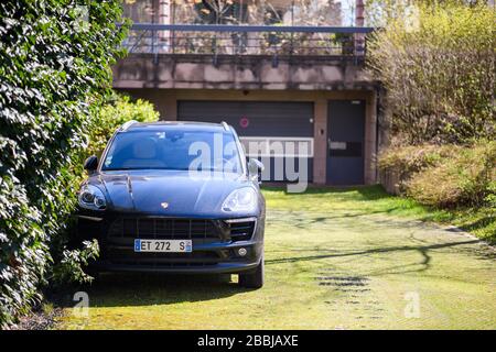 Strasburgo, Francia - 22 marzo 2020: Bella nuova Porsche Cayenne SUV parcheggiata di fronte alla grande porta garage verde erba piano Foto Stock