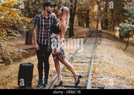 Una giovane coppia di amanti ha perso il treno. Un bacio sulle rotaie nella foresta d'autunno in attesa del prossimo treno. Foto Stock