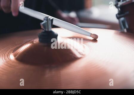 Primo piano della mano di un batterista che tiene i bastoni bianchi del tamburo mentre si siede dietro un set del tamburo. Foto Stock