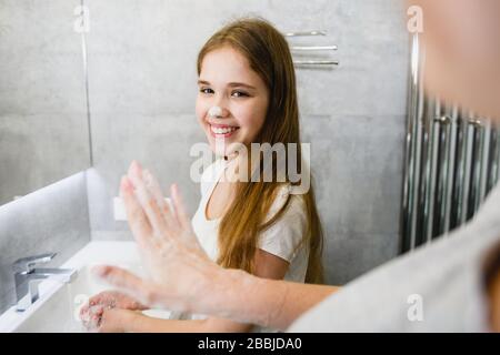 La madre e la figlia giocano durante il lavaggio delle mani vicino al lavandino e alla linguetta del bagno, la protezione contro virus e microbi durante il periodo dell'epidemia Foto Stock