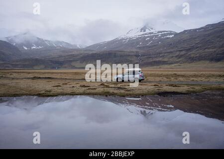 Auto che guida su strada ghiaia con riflessione in acqua, al crepuscolo Foto Stock