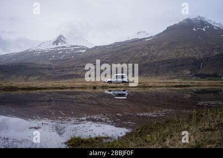 Auto che guida su strada ghiaia con riflessione in acqua, al crepuscolo Foto Stock