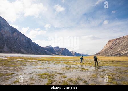Due backpackers attraversano la palude bagnata terra in Akshayak Pass. Foto Stock