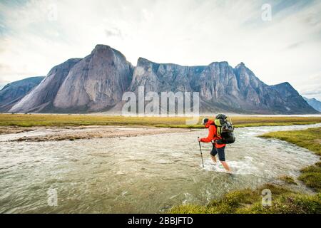 Backpacker attraversa il fiume sotto le montagne nel Passo di Akshayak Foto Stock