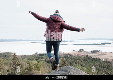 donna che salta da una roccia mentre escursioni con vista sull'oceano Foto Stock