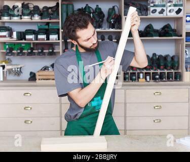 Il bottegaio portacolla in abiti da lavoro lavora in officina con dettagli in legno. Foto Stock