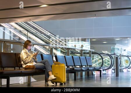 Donna sconvolto sopra la cancellazione del volo, scrive il messaggio alla famiglia, seduto in un terminal quasi vuoto aeroporto a causa di coronavirus pandemic/Covid-19 focolaio Foto Stock