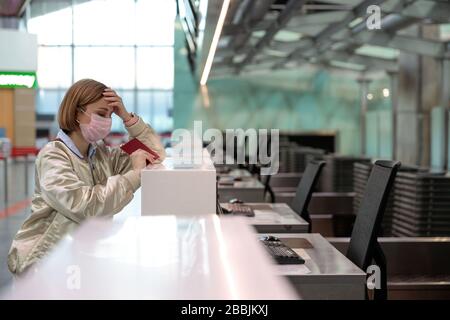 Donna con bagagli in caso di cancellazione del volo, si trova in banchi di check-in vuoti presso il terminal dell'aeroporto a causa di coronavirus pandemia/Covid-19 scoppio di traverve Foto Stock