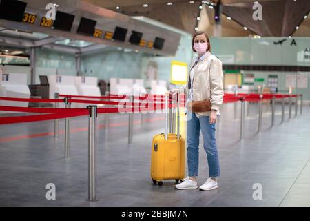 Donna con bagaglio si trova in banchi di check-in quasi vuoti presso il terminal dell'aeroporto a causa di coronavirus pandemic/Covid-19. Cancellazione del volo. Viaggi Foto Stock