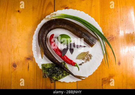 Garfish affumicato con lime, basilico, cipolle verdi, peperoncino, patatine, spezie, olio di oliva in un piatto bianco di ceramica, su un tavolo di legno Foto Stock