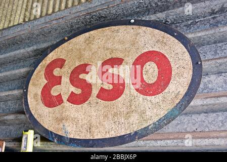 Vecchio segno di smalto per petrolio esso, pesantemente patinato, montato su ferro ondulato in officina Foto Stock