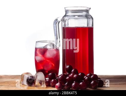 Composta di ciliegie in una brocca. Ciliegie su un tavolo di legno. Cubetti di ghiaccio. Una bevanda di frutta fredda in un bicchiere. Foto Stock