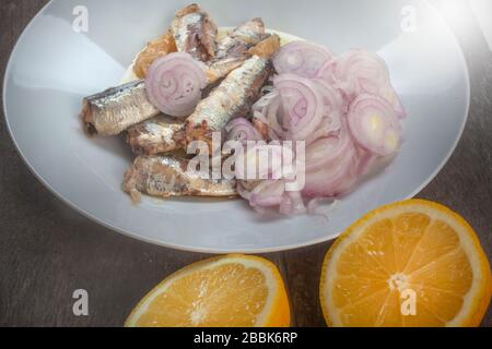 studio foto di sardinas con due limoni tagliati su una lastra bianca dalla composizione superiore su sfondo di legno Foto Stock