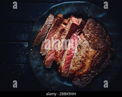 Deliziosa bistecca di Angus, di medie dimensioni, fatta in casa, di colore nero, con vista dall'alto su un piatto Foto Stock