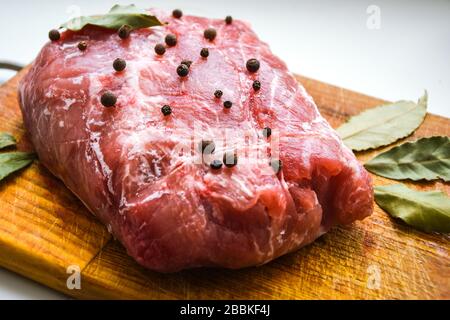 Spalla di maiale cruda con spezie. Foglia di baia, su uno sfondo di legno, primo piano, pepe nero su un pezzo fresco crudo di carne in spezie Foto Stock