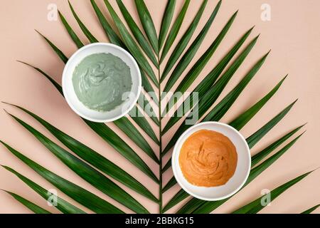 Maschere di argilla in ciotole e foglie tropicali su fondo di pesca. PRODOTTI cosmetici SPA per la cura della pelle del viso. Disposizione piatta, vista dall'alto Foto Stock