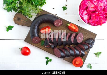 Morsilla - salsiccia di sangue. Pezzi di pudding nero spagnolo su una tavola da taglio in legno su sfondo bianco. Menu di Pasqua. Foto Stock