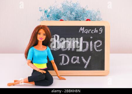 Tambov, Federazione russa - 24 febbraio 2020 Barbie con capelli castani seduto vicino a una lavagna con le parole Barbie Day marzo 9th. Studio. Foto Stock