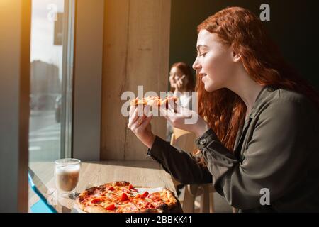 Modello femminile tiene un pezzo di pizza nelle sue mani. Giovane donna che mangia la pizza Foto Stock