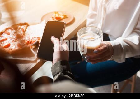 Giovane donna che fa un'immagine di una bevanda. Modello femminile che tiene un primo piano del telefono. Foto Stock
