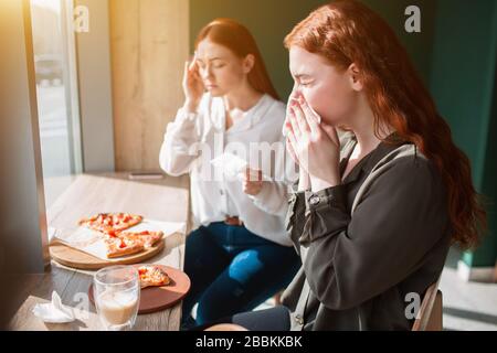 Modello femminile si siede in un caffè e soffia il suo naso. Giovane donna sente un mal di testa in un caffè. Foto Stock