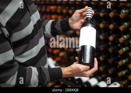 Primo piano di mano dell'uomo che tiene molto raro, vino di sughero rosso nell'enorme wine bar, degustazione di vino, concetto di bevanda Foto Stock