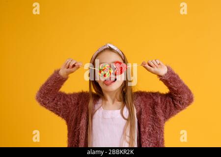 Bambina godere lollipop durante la pausa scolastica. Buon piccolo scolaretto mangiare lecca lecca. Ampie lollipop a vortice sulle avambracci Foto Stock