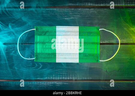 Maschera medica per la protezione contro le malattie aeree, dipinta nella bandiera nazionale della Nigeria su sfondo nero in fumo blu-verde. Prot. Medico Foto Stock